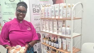 Ghanian woman in pink t-shirt holds a tray of soaps next to a stand of beauty products.  