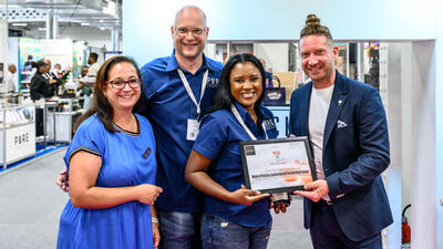 Two judges and two contestants stand smiling while holding winning certificate