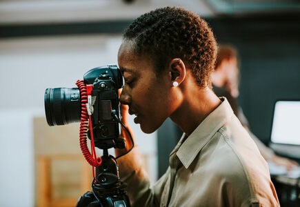 Side shot of woman looking through a camera lens which is on a tripod